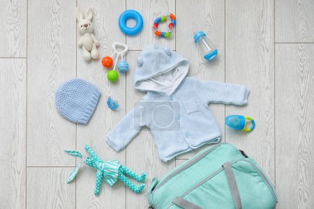 Foto de Elegante bolso con ropa y juguetes para bebé sobre fondo de madera clara - Imagen libre de derechos