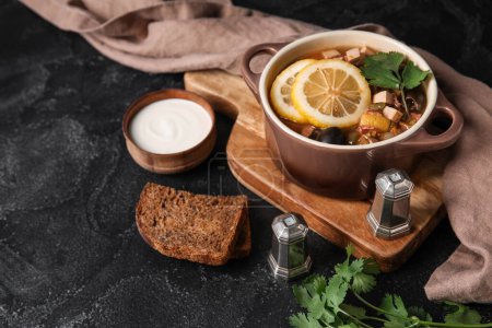 Téléchargez les photos : Pot de soupe Hodgepodge savoureuse avec du pain et de la crème sure sur fond sombre - en image libre de droit