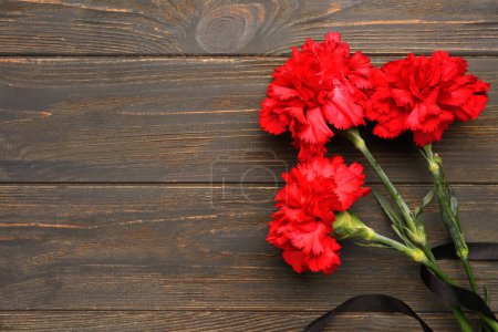 Photo for Red carnations and black ribbon on brown wooden background - Royalty Free Image