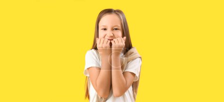 Foto de Little girl biting nails on yellow background - Imagen libre de derechos