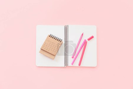 Flip paper calendar for June with notebook and pens on pink background