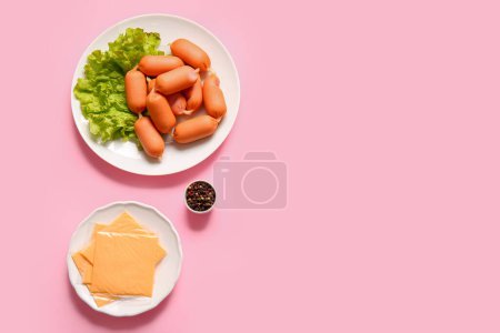 Plate of tasty boiled sausages with lettuce and cheese on pink background
