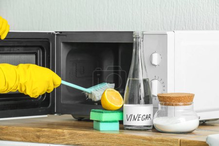 Téléchargez les photos : Femme de nettoyage four micro-ondes avec brosse, cuisson, bicarbonate de soude et vinaigre à la maison - en image libre de droit