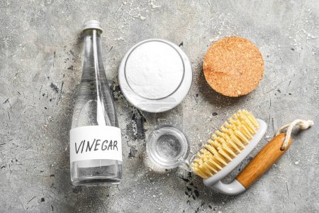 Bottle of vinegar, baking soda and brush on grunge background