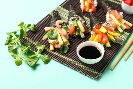 Photo for Bamboo mat with tasty sushi cones, soy sauce and lambs lettuce on color background, closeup - Royalty Free Image