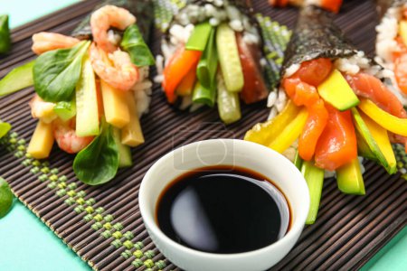 Foto de Estera de bambú con sabrosos conos de sushi y salsa de soja sobre fondo de color, primer plano - Imagen libre de derechos