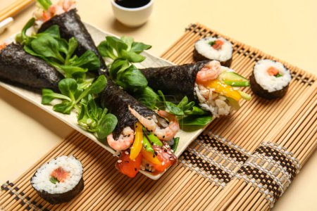 Foto de Placa con sabrosos conos de sushi, rollos, lechuga de cordero y estera de bambú sobre fondo de color, primer plano - Imagen libre de derechos