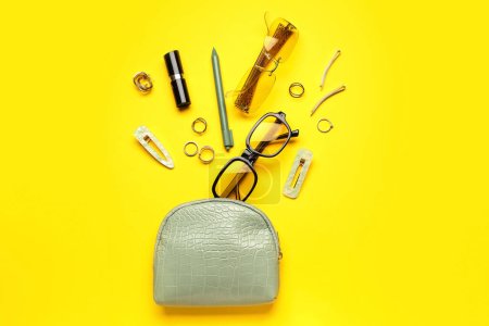 Kosmetiktasche mit Sonnenbrille und Accessoires auf gelbem Hintergrund