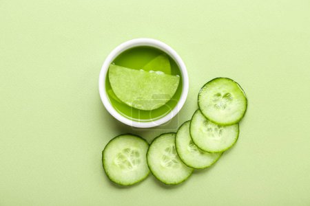 Photo for Bowl with cotton under-eye patches and cucumber slices on green background - Royalty Free Image