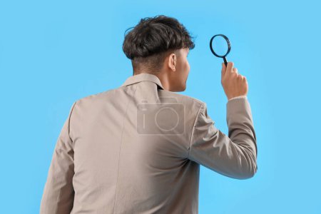 Photo for Young man with magnifier on blue background, back view - Royalty Free Image