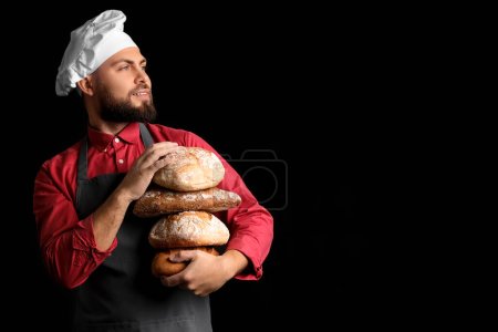 Foto de Panadero masculino con panes de pan fresco sobre fondo oscuro - Imagen libre de derechos