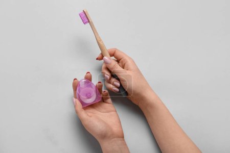 Téléchargez les photos : Main féminine avec fil dentaire et brosse à dents en bambou violet sur fond gris - en image libre de droit