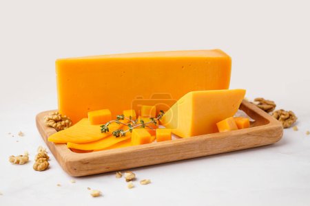 Foto de Tablero de madera con sabroso queso cheddar sobre fondo claro - Imagen libre de derechos