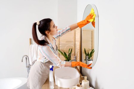 Téléchargez les photos : Jeune femme nettoyage miroir dans sa salle de bain - en image libre de droit