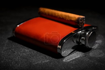 Téléchargez les photos : Nouveau flacon de hanche avec cigare sur fond sombre - en image libre de droit