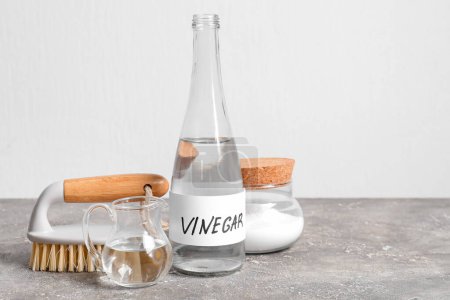 Bottle of vinegar, baking soda and brush on table near light wall