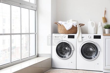 Photo for Basket with dirty clothes and detergent on washing machines in laundry room - Royalty Free Image
