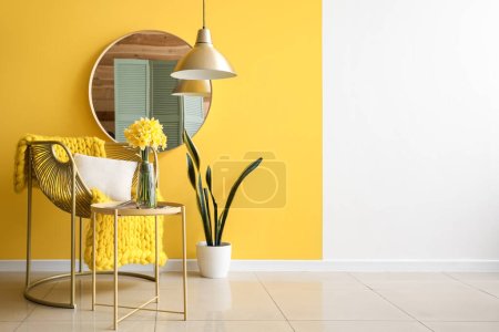 Foto de Elegante sillón, jarrón con flores narcisas florecientes en la mesa de café y espejo cerca de la pared amarilla - Imagen libre de derechos