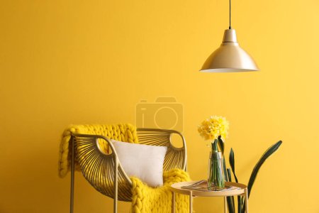 Foto de Elegante sillón y jarrón con flores narcisas florecientes en la mesa de café cerca de la pared amarilla - Imagen libre de derechos