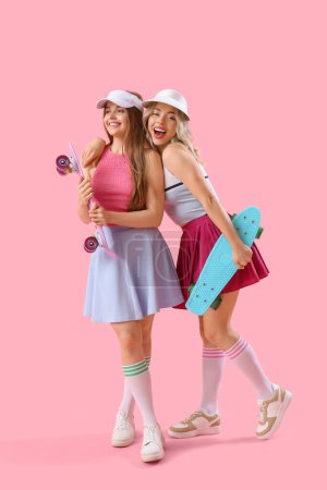 Foto de Hermanas jóvenes con monopatines sobre fondo rosa - Imagen libre de derechos