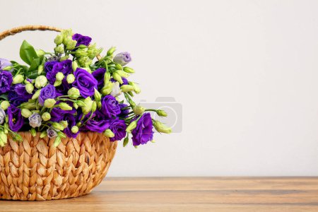 Basket with eustoma flowers on wooden table near white wall