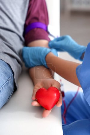 Young man with heart donating blood in clinic, closeup