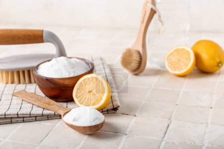 Foto de Cuchara con bicarbonato de sodio, limones, cepillos de limpieza y servilleta en la mesa de baldosas ligeras - Imagen libre de derechos