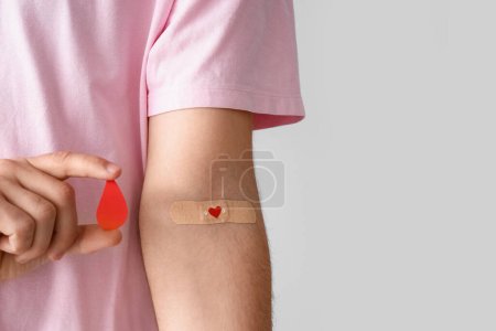 Young blood donor with applied medical patch and paper drop on light background, closeup