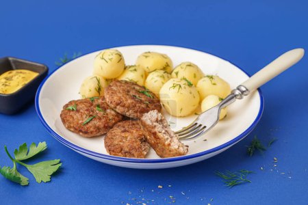 Plate with cutlets, boiled baby potatoes and dill on blue background