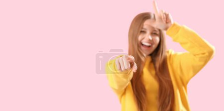 Foto de Mujer joven mostrando gesto perdedor y apuntando al espectador sobre fondo rosa con espacio para el texto - Imagen libre de derechos