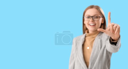 Photo for Laughing young businesswoman showing loser gesture on light blue background with space for text - Royalty Free Image