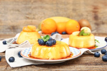 Téléchargez les photos : Assiettes de délicieux puddings aux fruits et bleuets recouverts de sirop de caramel sur table en bois - en image libre de droit
