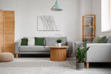 Innenraum eines hellen Wohnzimmers mit grauen Sofas und Zimmerpflanze auf Couchtisch