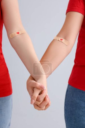 Téléchargez les photos : Donneuses de sang avec des patchs médicaux appliqués tenant les mains sur fond clair, gros plan - en image libre de droit