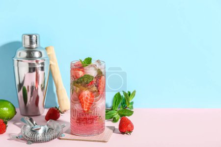 Téléchargez les photos : Verre de fraise fraîche mojito avec shaker, passoire et ingrédients sur table rose près du mur bleu - en image libre de droit