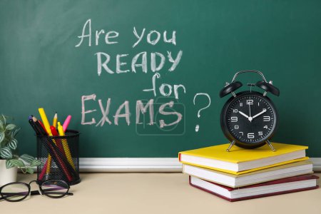 Photo for Alarm clock, books and pen holder on table against blackboard with question ARE YOU READY FOR EXAMS? - Royalty Free Image