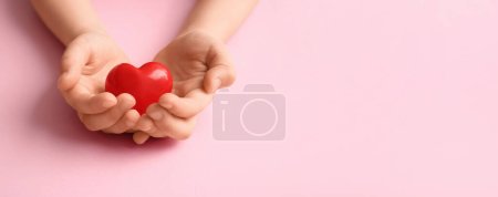 Foto de Manos de niño con corazón rojo sobre fondo rosa con espacio para texto - Imagen libre de derechos