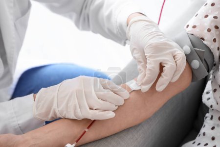 Female doctor taking young donor's blood in clinic, closeup