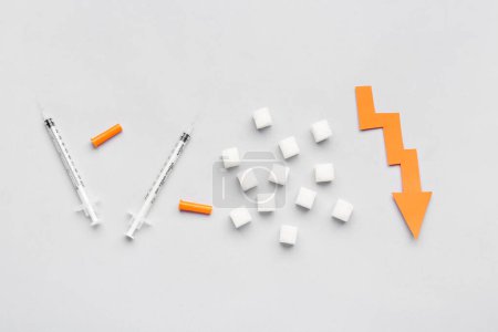 Téléchargez les photos : Cubes de sucre avec seringues pour injection d'insuline et flèche dirigée vers le bas sur fond blanc - en image libre de droit