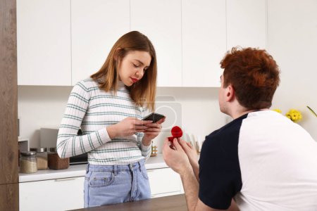 Photo for Young woman with mobile phone get proposed in kitchen - Royalty Free Image