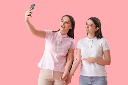 Téléchargez les photos : Donneuses de sang avec des patchs appliqués prenant selfie sur fond rose - en image libre de droit