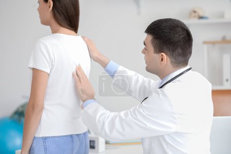 Männlicher Arzt überprüft Haltung junger Frau in Klinik