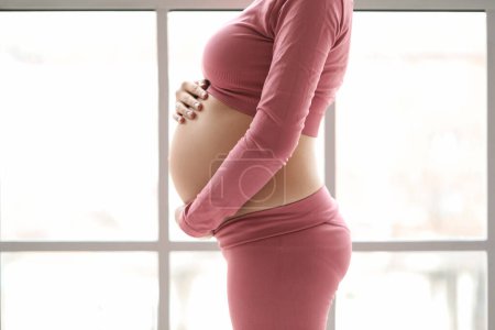 Photo for Sporty pregnant woman near window at home, closeup - Royalty Free Image