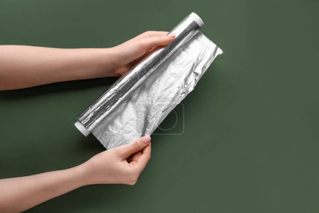Photo for Female hands with roll of aluminium foil on green background - Royalty Free Image