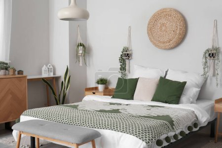 Photo for Interior of light bedroom with cozy bed, wooden cabinet and hanging houseplants - Royalty Free Image