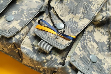 Chain with Ukrainian coat of arms, ribbons and military bag on yellow background, closeup