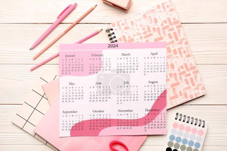Calendario, cuadernos, paleta de colores y papelería sobre fondo de madera blanca