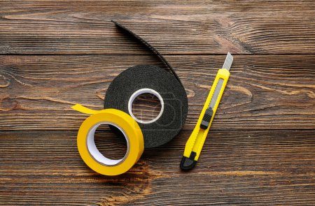 Photo for Adhesive tape rolls and stationery knife on wooden background - Royalty Free Image