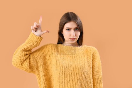 Photo for Young woman showing loser gesture on beige background - Royalty Free Image