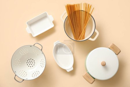 Foto de Set de utensilios de cocina y olla con pasta cruda sobre fondo beige - Imagen libre de derechos